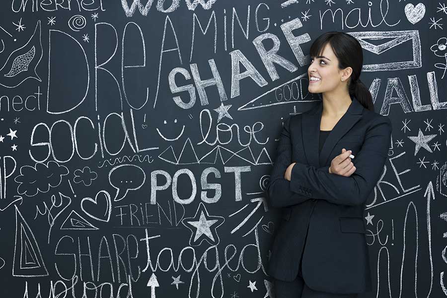 una ragazza sorridente di fronte ad una lavagna sulla quale sono scritti termini correlati ai social: Gestione social network secondo Creativi Digitali