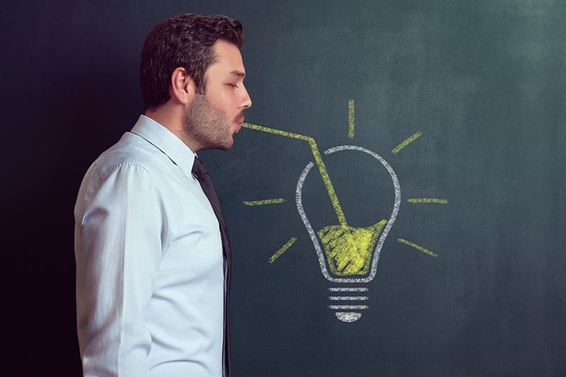 un uomo fa finta di bere da una cannuccia disegnata all'interno di una lampadina, anch'essa disegnata su di una lavagna. Produzione di video aziendali: perchè attingere da un'agenzia creativa