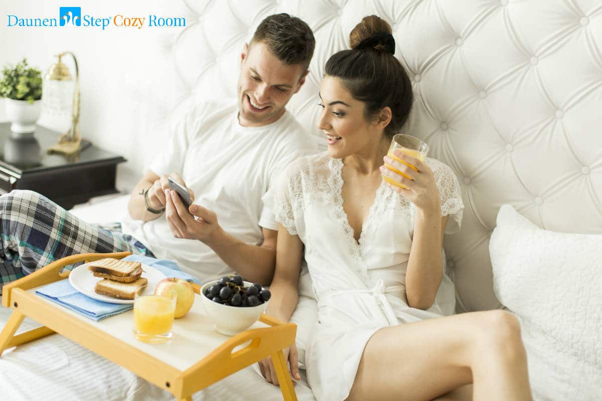 Social Game "DaunenStep Cozy Room" - coppia a letto, fa colazione controllando il cellulare