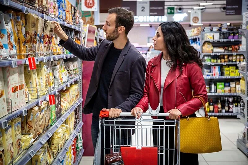 Coppia con carrello della spesa tra gli scaffali di un supermercato