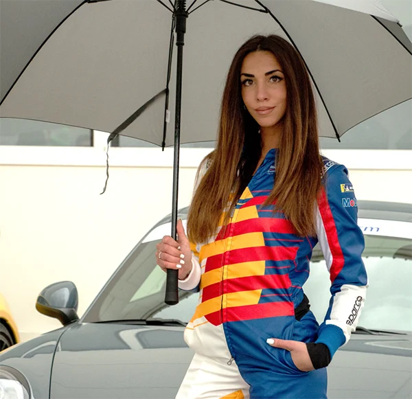 Hostess in tuta racing con ombrello accanto a un’auto
